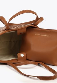 Brown leather tote bag with textured exterior, interior pocket, and matching handles. Gold hardware detail and stitched accents.