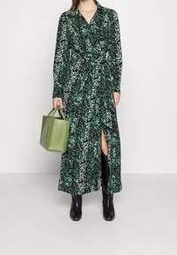 Grön och svart leopardmönstrad lång klänning med knytmidja, delad kjol och långa ärmar; kombinerad med en liten grön läderväska och svarta stövlar.