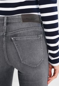 Szare dżinsy z denimu o średnim stanie. Posiadają skórzaną metkę marki oraz trzy tylne kieszenie z delikatnymi detalami w postaci szwów.