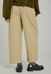 Beiga vida byxor med en slät yta, hög midja och sidofickor. I kombination med mörka loafers och grå strumpor.