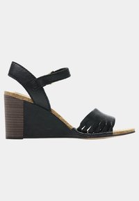 Sandales à semelle en liège noires à talon compensé, à bout ouvert, avec des détails en frange sur le devant. Bride de cheville avec une boucle métallique en accent.