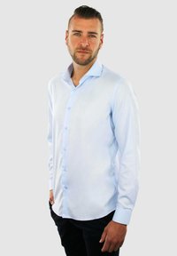 Lichtblauw overhemd met lange mouwen, knoopsluiting aan de voorkant, zachte textuur, gespreide kraag en ronde zoom, gecombineerd met donkere broek.