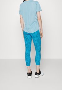 Maglietta sportiva azzurro chiaro abbinata a leggings blu brillante con un motivo a macchie nere, indossati con sneakers nere.