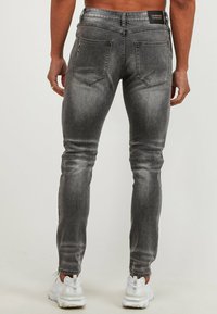 Vaqueros de mezclilla gris de corte ajustado con acabado desgastado, cinco bolsillos, costuras reforzadas y una etiqueta con el logo en la cintura.