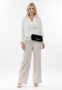 Cowl-neck white top, beige wide-leg trousers, black clutch with silver accent, and white strappy heels, presented against a white background.