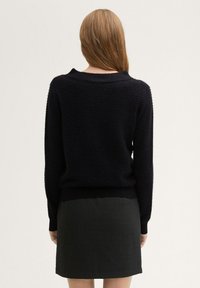 Schwarzer strukturierten Pullover mit rundem Ausschnitt und langen Ärmeln, kombiniert mit einem dunklen strukturierten Rock. Beide haben eine taillierte Passform.