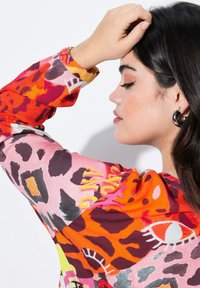 Blouse colorée et à motifs avec des teintes de rose, orange et noir, de coupe ample. Le tissu a une texture lisse, des manches longues avec des détails de poignet.