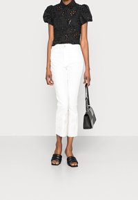 Sort bluse i blonde med puffærmer, hvide cropped bukser med blomsterbroderi, sorte sandaler og en sort håndtaske. Glatte teksturer gennem hele looket.