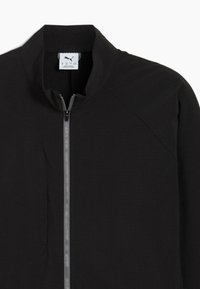 Svart zip-jacka med en strukturerad tyg och ståkrage, med en grå dragkedja och en liten logotypmärke nära kragen.
