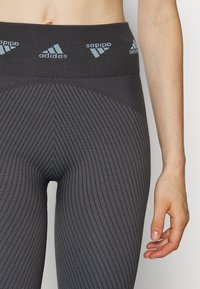 Gray athletic leggings featuring a textured, vertical ribbed pattern, a high waistband with light blue Adidas branding on top.
