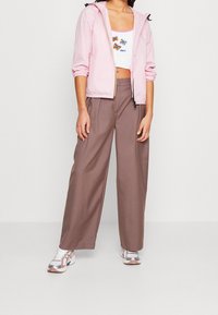 Rosa letvægts zip-up jakke, løse brune bukser og multicolore sneakers. Hvid crop top med sommerfugle-broderi og "Obey" tekst.