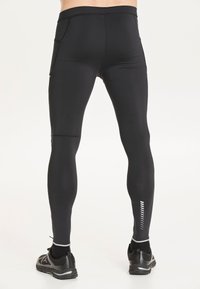 Svarta atletiska leggings med en åtsittande design, utrustade med två sidofickor och en reflekterande detalj längs underbenet. Texturerad midja.