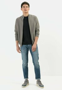 Szara bomberka na zamek błyskawiczny noszona na czarnej koszulce, połączona z dżinsami z podwiniętymi nogawkami i szarymi sneakersami z kremowymi akcentami.