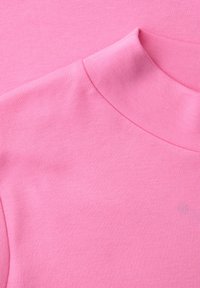 Gros plan d'un tissu rose doux montrant un col montant plié et une texture lisse sur un vêtement.