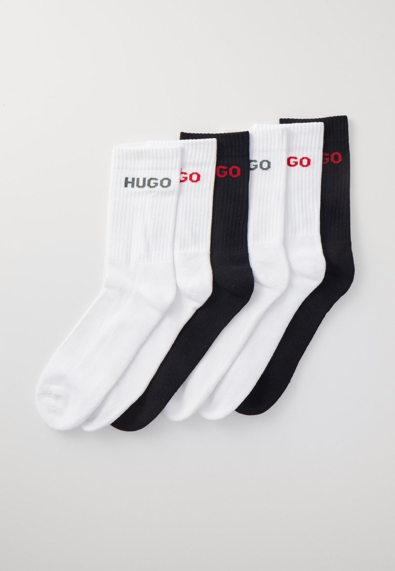 Négy pár pamut zokni fekete és fehér színben, bordázott textúrával, a "HUGO" szürke logóval és a "GO" piros logóval.