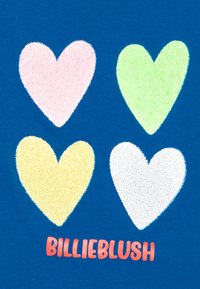 Blå T-skjorte med fire teksturerte hjerter i rosa, grønn, gul og hvit, med "BILLIEBLUSH" trykket i oransje nederst.