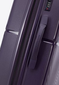 Valigia rigida viola con una superficie testurizzata, dotata di chiusura con zip, manico moldato e serratura a combinazione sul lato.