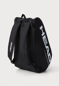 Mochila negra con dos correas de hombro acolchadas y un asa en la parte superior. Presenta un bolsillo con cremallera y una gran marca blanca en el lateral.