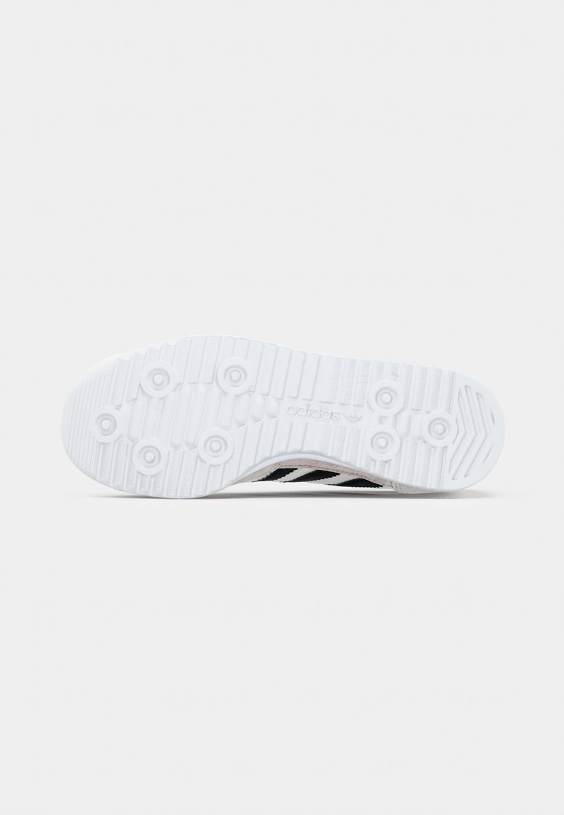 Semelle de chaussure blanche avec surface texturée, comprenant trois bandes noires et des motifs circulaires pour l'adhérence. Design épuré et minimaliste.