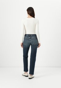White long-sleeve top paired with dark blue high-waisted jeans. Smooth fabric texture, simple design, and classic five-pocket style.