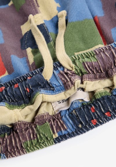 Gros plan sur un tissu camouflage multicolore avec des cordons beiges et un détail de taille élastique sur un vêtement.