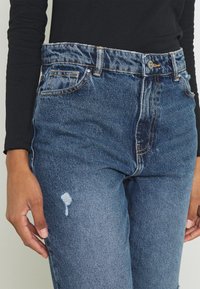 Högmidjade blå denimjeans med en urtvättad finish, med slitna detaljer på låret och en klassisk femfickdesign.