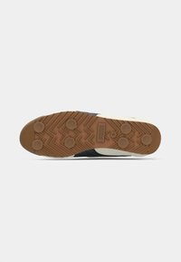 Sneaker sål i gummi med brun trækkraftsmønster. Har en hvid mellemsål og sorte accenter på de øverste sektioner. Flad og struktureret design.
