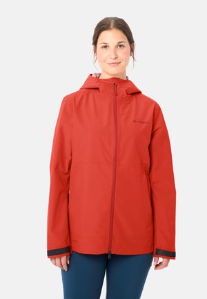 Donna che indossa una giacca impermeabile rossa con cerniera frontale e cappuccio, in piedi contro uno sfondo chiaro uniforme.