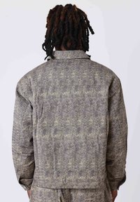 Veste grise à motifs avec un col et des manches longues, présentant un tissu texturé et des détails de couture le long des coutures.