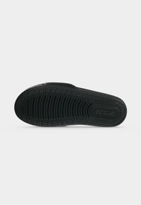 Μαύρη σόλα σανδαλιού Crocs με υφή λαβής και ανάγλυφο όνομα της μάρκας σε απλό λευκό φόντο.