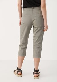 Šedé sáčko kalhoty s hladkou texturou, které mají zadní kapsy a ohrnuté lemy, v kombinaci s černými sandály na ploché podrážce s pásky.