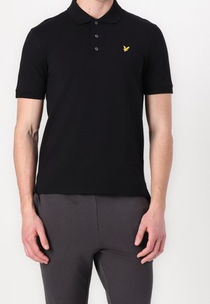Polo noir en coton avec col, manches courtes et logo brodé jaune sur la poitrine gauche.