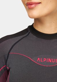 Czarna termiczna bluzka o prążkowanej teksturze, z czerwonym logo "ALPINUS" i zaokrąglonymi różowymi akcentami wzdłuż szwów na ramionach.