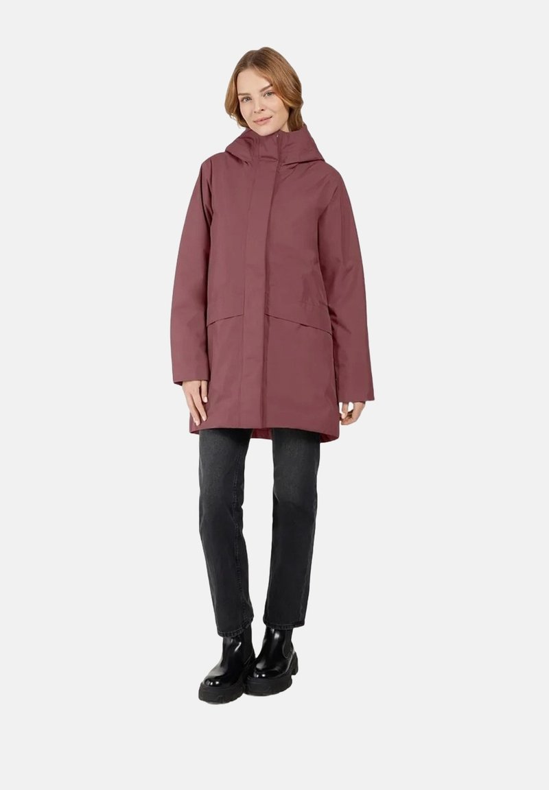 Bordeauxfarbene wasserdichte Jacke mit Kapuze, Frontreißverschluss und zwei großen Seitentaschen. Kombiniert mit schwarzen Jeans und glänzenden schwarzen Stiefeln.