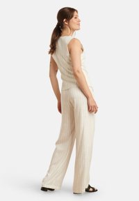Hellbeige ärmelloses Oberteil mit vertikalen Streifen, kombiniert mit weiten Hosen, die dasselbe Muster aufweisen. Das Material wirkt strukturiert. Schwarze Blockabsatzsandalen.