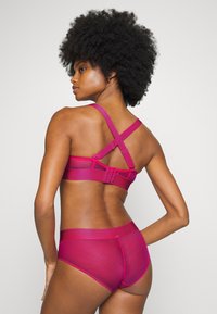 Sutiã fúcsia com alças cruzadas e fecho ajustável, combinado com uma cueca correspondente. Tecido suave com um design semi-translúcido.