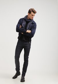 Marine bomberjakke, sort turtleneck, mørke denim jeans og sorte læder ankle boots. Modellen bærer et struktureret marinefarvet tørklæde.