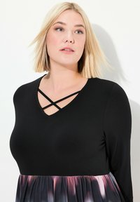Svart långärmad topp med V-ringning och korsbanddetalj, som har en flödande gradientkjol i nyanser av lila och rosa.