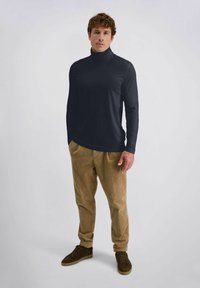 Dunkelblaues Rollkragen-Shirt aus glattem Stoff, taillierter Schnitt mit langen Ärmeln, kombiniert mit hellbraunen Kordhosen und schwarzen Sneakers.