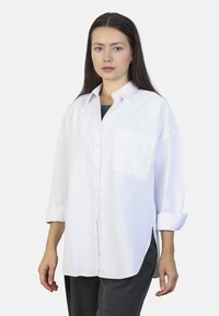 White button-up shirt with a chest pocket, rolled-up sleeves, and a relaxed fit. Made from smooth fabric, features a classic collar.