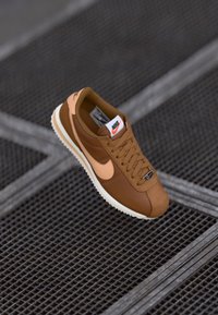 Smešani smeđi tenisice s bež detaljima, izrađene od kože i antilopa, okrugli vrh, strukturirana potplata i istaknuti Nike logo na jeziku.