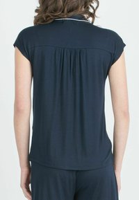 Top corto a maniche corte di colore blu navy in morbido tessuto, con retro plissettato, colletto e orlo leggermente curvo. Adatto per un abbigliamento casual.