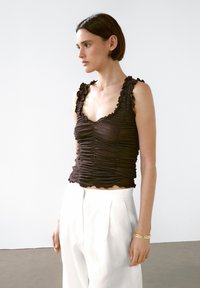 Hnědý, přiléhavý top s nařaseným designem a vykrojenými okraji. Nosit s bílými kalhotami s vysokým pasem. Jednoduchá, elegantní silueta.