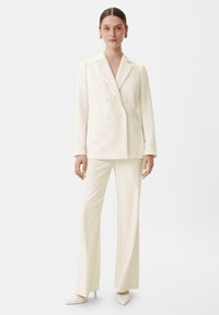 Cream-colored double-breasted blazer with textured fabric, paired with matching wide-leg trousers and pointed-toe heels. Minimalist design.