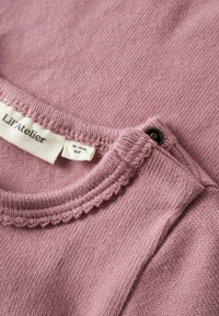 Gaiši rozā adīts tops ar noapaļotu kakla izgriezumu, kuram ir viļņota mala un pogu detaļa. Etiķetē norādīta izmēra 4-6M.