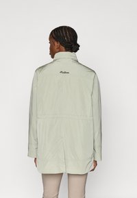 Ανοιχτό πράσινο μπουφάν με ψηλό γιακά, μακριά μανίκια και κεντημένο λογότυπο στο πάνω μέρος της πλάτης. Διαθέτει άνετη εφαρμογή και λεία υφή.