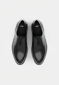 Black leather dress shoes with a smooth finish, rounded toe, lace-up design, and subtle stitching details. Logo appears on the insole.