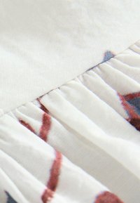 Biała tkanina o delikatnym połysku, z marszczonymi sekcjami i abstrakcyjnymi wzorami w ziemistych odcieniach, nadającymi miękką teksturę.