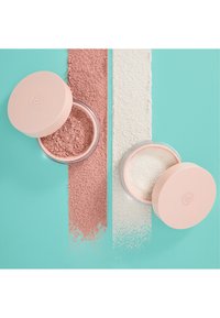 Deux contenants ouverts de poudre libre pour maquillage, l'un rose et l'autre blanc, avec des échantillons de poudre assortis sur un fond turquoise.