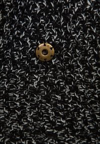 Tissu en tricot noir et blanc avec un motif texturé, comprenant un bouton rond en laiton avec un trou central cousu dans la maille.